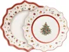 Two Christmas-themed plates are shown, one partially overlapping the other. The plate in the foreground has a Christmas tree design in the center, while the plate in the background has a festive pattern of toys and gifts. Náhled obrázku produktu