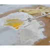 A close-up shot of a whisk attachment for a hand mixer placed in a pile of flour with an egg yolk in the center. In the background, there is a pile of uncooked pasta. Anteprima dell’immagine prodotto