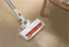A cordless vacuum cleaner head with a red brush roll is shown cleaning a wooden floor, with some dust visible on the floor. Produktbild-Vorschau