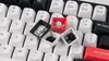 A close-up view of a mechanical keyboard with several keycaps removed, revealing the switches underneath. Some keycaps are scattered around the keyboard. Produktbild-Vorschau