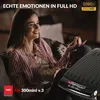 A woman is sitting on a couch watching TV and eating popcorn. A set-top box is in the foreground. Produktbild-Vorschau