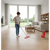 A woman is mopping the floor in a bright, modern living room with large windows. Produktbild-Vorschau