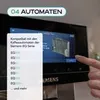 A close-up of a coffee machine's touchscreen display showing compatibility information, with a finger pointing to the screen. Produktbild-Vorschau