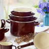 A stack of brown enamel pots and a single pot with a handle are arranged on a white surface, with a vase of blue flowers and dried flax stems in the background. Voir les images du produit