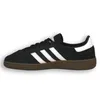 A side view of a black Adidas Handball Spezial sneaker with white stripes and a brown sole, isolated on a white background. Voir les images du produit