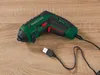 A cordless screwdriver with a USB charging cable on a wooden surface. Produktbild-Vorschau