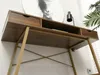 A close-up, low-angle view of a modern desk with a wooden top and gold metal legs, set against a white wall with a piece of abstract art in the background. Voir les images du produit