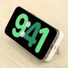 A smartphone with a large green digital clock display is shown on a wooden surface, propped up by a white accessory. Voir les images du produit
