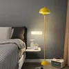 A yellow floor lamp stands next to a bed in a bedroom. Produktbild-Vorschau