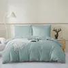 A neatly made bed with a sage green duvet cover and two pillowcases, a white throw blanket, and a book on the bed. Podgląd zdjęcia produktu