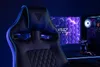 A gaming chair is shown in a dimly lit room with a computer monitor displaying a hexagonal pattern. Produktbild-Vorschau