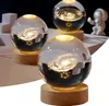 Three illuminated crystal spheres with galaxy and solar system engravings, each on a wooden base, with a small astronaut figurine in the background. Produktbild-Vorschau