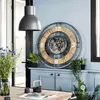 A large decorative clock with a visible mechanism is mounted on a light blue wall above a blue cabinet. Several potted plants are placed on the cabinet and a table in the foreground. Náhľad obrázku produktu