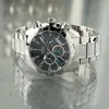 A close-up shot of a men's chronograph watch with a black dial and silver band, resting on a reflective surface. Náhľad obrázku produktu