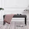 A gray upholstered bench with a striped throw blanket and magazines on it, placed on a patterned rug in a room with white decorative molding on the wall. Náhled obrázku produktu