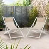 Two beige and white folding lounge chairs are set up on a patio with a wooden fence and greenery in the background. Produktbild-Vorschau
