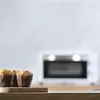 Three muffins in brown paper wrappers sit on a wooden board in front of a blurred white oven. Produktbild-Vorschau