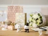 Wedding-themed display with bride and groom figurines, gifts, and flowers. Produktbild-Vorschau