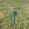 A close-up shot of a green screw-in ground stake with a wire attached, driven into grass. Anteprima dell’immagine prodotto