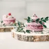 Two pink macarons decorated with greenery and small white flowers, displayed on wooden slices. Produktbild-Vorschau