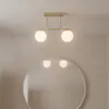 A modern gold ceiling light with two white glass globes is shown above a round mirror reflecting the light. Náhľad obrázku produktu