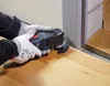 A person wearing gloves is using a Bosch oscillating tool to cut along a door frame. Podgląd zdjęcia produktu