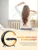 A woman waking up in bed with a sunrise alarm clock in the foreground. Produktbild-Vorschau