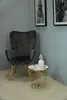 A dark gray armchair sits next to a small round side table with a decorative pineapple on it. Produktbild-Vorschau