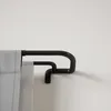 A close-up view of a black double curtain rod mounted on a white wall, with a light gray curtain hanging from it. Podgląd zdjęcia produktu
