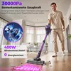 A man is using a purple cordless vacuum cleaner in a living room. Produktbild-Vorschau