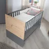 A baby crib in a room with a window and curtains in the background. Produktbild-Vorschau