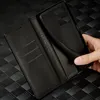 A hand is holding a black leather phone case open, revealing the inside compartments and the phone holder. Produktbild-Vorschau