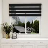 A window with black and white striped blinds, showing a mountain landscape with houses. Produktbild-Vorschau