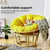 A yellow papasan chair with cushions and a throw blanket, placed in a room with a plant and rug. Produktbild-Vorschau