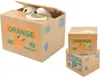 A coin-collecting cat toy sits inside a cardboard box labeled 'ORANGE' and 'Southland'. Two smaller boxes, one labeled 'ORANGE' and another 'BIG GRAPE', are stacked to the right. Anteprima dell’immagine prodotto