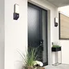Exterior view of a modern house with a black door and wall-mounted lights. Produktbild-Vorschau