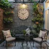 A cozy outdoor seating area with a large wall clock, a bench, chairs, and plants. Anteprima dell’immagine prodotto