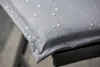 Close-up of a gray cushion with water droplets on it, resting on a black metal frame. Produktbild-Vorschau