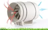 A white inline duct fan is shown on a white surface with green grass at the bottom. Red arrows indicate air entering the fan, and blue arrows indicate air exiting. Náhled obrázku produktu