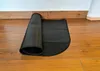 A black mat is partially unrolled on a wooden floor, next to a white wall. Náhled obrázku produktu