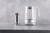 A glass electric kettle and a metal tea infuser are placed on a gray countertop against a textured gray background. Náhled obrázku produktu