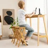 A woman sits at a high table, with two bamboo bar stools in the foreground. Produktbild-Vorschau