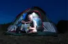A man is sitting inside a tent at night, looking at a map under the light of a hanging LED lamp. Voir les images du produit
