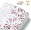 A close-up, angled view of a quilted white textile product with a pink rose pattern, featuring certification logos and text in the upper right corner. Produktbild-Vorschau