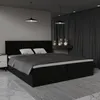 A modern black upholstered bed with white pillows, set in a dimly lit bedroom with dark curtains and pendant lights. Produktbild-Vorschau