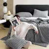 A woman is sitting on the floor in front of a bed, holding a magazine. She is surrounded by soft, plush blankets and pillows. Produktbild-Vorschau