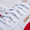 A close-up view of the front of a white Puma sneaker with gold branding and a red accent. Produktbild-Vorschau