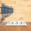 A set of wrenches is mounted on a wooden wall above a white power strip with three outlets on a wooden surface. Produktbild-Vorschau