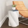 A white ceramic stool with a spiral design sits next to an orange lounge chair in a room with textured walls and dark wood flooring. Anteprima dell’immagine prodotto