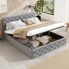 A bedroom scene featuring a grey upholstered bed with its storage compartment open, revealing stored items. The bed is made with white and beige bedding and pillows. A plant and a window with greenery are visible in the background. Anteprima dell’immagine prodotto